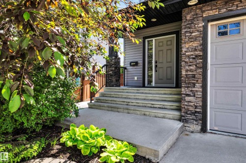 Exterior featuring stacked stone accents, horizontal siding, a paneled entry door with sidelight, concrete steps, and an attached garage with panel door - 18 Voleta Crest, Spruce Grove, AB 