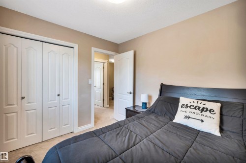 Neutral-toned bedroom featuring bi-fold closet doors, light-colored carpeting, and a contrasting dark wood-finish headboard - 18 Voleta Crest, Spruce Grove, AB 