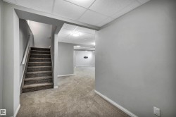 Carpeted staircase with white handrail leading to a finished lower level with recessed lighting, drop ceiling, and light gray wall paint - 