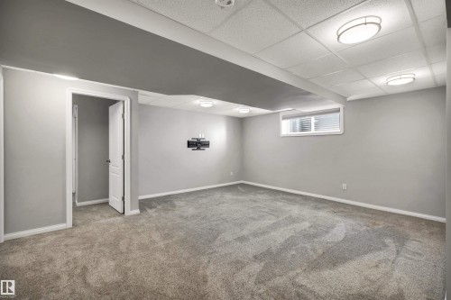 Spacious room featuring neutral gray walls, gray carpeting, a drop ceiling with integrated lighting, white trim, and a window with blinds - 18 Voleta Crest, Spruce Grove, AB 