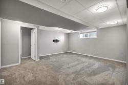 Spacious room featuring neutral gray walls, gray carpeting, a drop ceiling with integrated lighting, white trim, and a window with blinds - 