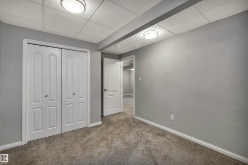 Room featuring light gray walls, gray carpet flooring, white bi-fold closet doors, white baseboards, and a drop ceiling with integrated lighting - 18 Voleta Crest, Spruce Grove, AB 