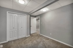 Room featuring light gray walls, gray carpet flooring, white bi-fold closet doors, white baseboards, and a drop ceiling with integrated lighting - 