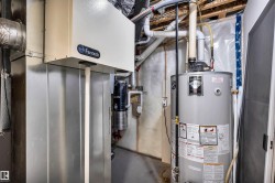 Mechanical room featuring a water heater, furnace, and exposed overhead piping - 
