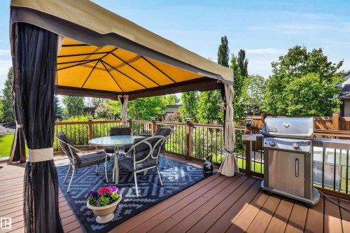 Spacious outdoor deck featuring rich wood-finish flooring, a dark wood railing with black metal balusters, and a yellow-canopied gazebo with black mesh privacy curtains - 18 Voleta Crest, Spruce Grove, AB 