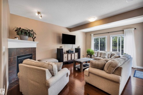Living area featuring rich wood-finish flooring, a built-in fireplace with tile surround and white mantel, and ample natural light through multiple windows - 18 Voleta Crest, Spruce Grove, AB 