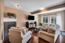 Living area featuring rich wood-finish flooring, a built-in fireplace with tile surround and white mantel, and ample natural light through multiple windows - 18 Voleta Crest, Spruce Grove, AB 