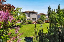 Expansive rear yard featuring a manicured lawn, mature trees, flowering shrubs, and a built-in deck with a privacy screen - 