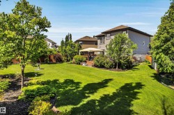 Spacious backyard featuring a large green lawn, mature trees, landscaped garden beds, a wooden deck, and a privacy fence - 