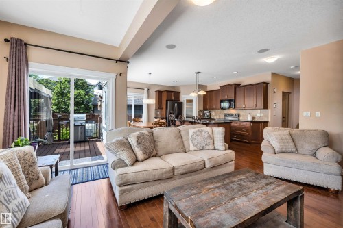 Open-concept living area featuring rich wood-finish flooring, a contemporary kitchen with dark cabinetry and black appliances, and direct access to an outdoor deck through sliding glass doors - 18 Voleta Crest, Spruce Grove, AB 