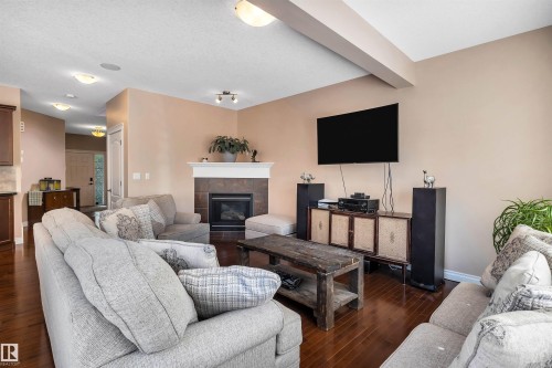 Living area featuring rich wood-finish flooring, a contemporary fireplace with a tile surround and white mantel, and ceiling-mounted light fixtures - 18 Voleta Crest, Spruce Grove, AB 
