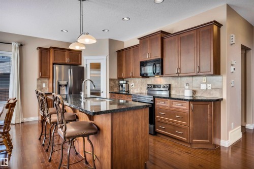 Kitchen featuring dark wood cabinetry, stainless steel appliances, a center island with a sink, and pendant lighting - 18 Voleta Crest, Spruce Grove, AB 
