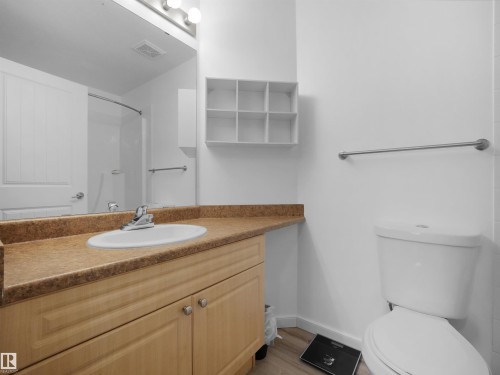 Bathroom featuring a wood-finish vanity with a built-in sink, a speckled countertop, and a large mirror - #217 240 Spruce Ridge Rd, Spruce Grove, AB - Indoor Photo Showing Bathroom