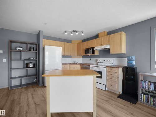 Kitchen featuring wood-finish flooring, a central island with a light wood countertop, light wood cabinetry, white appliances, and a white tile backsplash - #217 240 Spruce Ridge Rd, Spruce Grove, AB - Indoor Photo Showing Kitchen