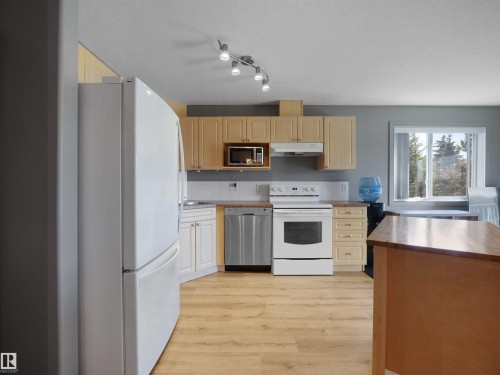Kitchen featuring wood-finish flooring, light wood cabinetry, white appliances, and a window - #217 240 Spruce Ridge Rd, Spruce Grove, AB - Indoor Photo Showing Kitchen
