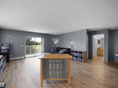 Bright living area featuring wood-finish flooring, a sliding glass door to a private balcony, and ample natural light - #217 240 Spruce Ridge Rd, Spruce Grove, AB - Indoor Photo Showing Living Room