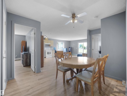 Spacious open-concept living area featuring wood-finish flooring, light gray wall tones, and a ceiling fan with integrated lighting - #217 240 Spruce Ridge Rd, Spruce Grove, AB - Indoor Photo Showing Dining Room