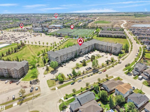 Multi-story residential building with light-colored siding and dark roofing, featuring a surface parking lot - #217 240 Spruce Ridge Rd, Spruce Grove, AB - Outdoor With View