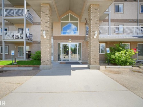 Building entrance featuring double glass doors, brick columns, and an arched transom window - #217 240 Spruce Ridge Rd, Spruce Grove, AB - Outdoor With Balcony With Facade
