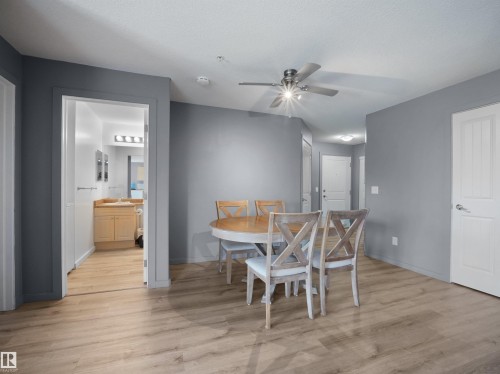 Open-concept living area featuring wood-finish flooring, a ceiling fan with integrated lighting, and a neutral gray wall palette - #217 240 Spruce Ridge Rd, Spruce Grove, AB - Indoor Photo Showing Dining Room