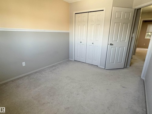 Carpeted room featuring a two-tone wall treatment with a chair rail, a bi-fold closet door, and a paneled entry door - 21354 87A Avenue, Edmonton, AB 