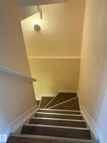 Staircase featuring wood-finish treads with silver-tone nosing, white baseboards, and a white wall-mounted handrail - 21354 87A Avenue, Edmonton, AB 