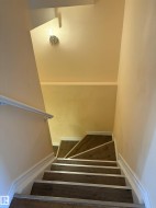 Staircase featuring wood-finish treads with silver-tone nosing, white baseboards, and a white wall-mounted handrail - 