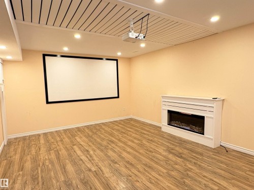 Spacious entertainment room featuring a large projector screen, ceiling-mounted projector, decorative fireplace with mantel, recessed lighting, and wood-finish flooring - 21354 87A Avenue, Edmonton, AB 