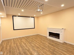 Spacious entertainment room featuring a large projector screen, ceiling-mounted projector, decorative fireplace with mantel, recessed lighting, and wood-finish flooring - 