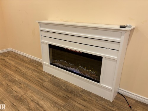 Integrated white electric fireplace with hearth and mantel, set against neutral wall tones and complementing wood-finish flooring - 21354 87A Avenue, Edmonton, AB 