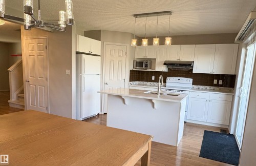 Open-concept kitchen featuring white cabinetry, a central island with a sink, a brown tiled backsplash, and recessed lighting - 21354 87A Avenue, Edmonton, AB 