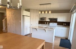 Open-concept kitchen featuring white cabinetry, a central island with a sink, a brown tiled backsplash, and recessed lighting - 