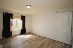 Spacious room featuring wood-finish flooring, a large window, and a white paneled door with brushed nickel hardware - 