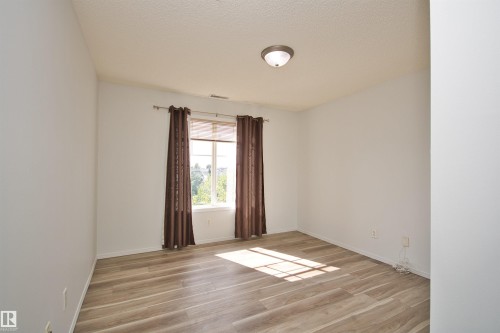 Spacious room with light wood-finish flooring, a contemporary flush-mount ceiling light fixture, and a large window providing ambient light - 311 2098 Blackmud Creek Drive, Edmonton, AB 