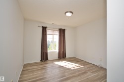 Spacious room with light wood-finish flooring, a contemporary flush-mount ceiling light fixture, and a large window providing ambient light - 