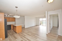 Spacious open-concept living area featuring wood-finish flooring, a kitchen island with seating, pendant lighting, and abundant natural light from the sliding glass door leading to a balcony - 