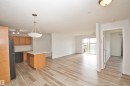 Spacious open-concept living area featuring wood-finish flooring, a kitchen island with seating, pendant lighting, and abundant natural light from the sliding glass door leading to a balcony - 311 2098 Blackmud Creek Drive, Edmonton, AB 