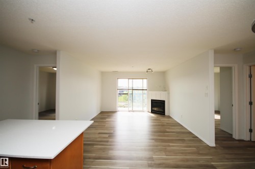 Open-concept living space featuring wood-finish flooring, a contemporary fireplace with a white mantel, and a sliding glass door to an outdoor area - 311 2098 Blackmud Creek Drive, Edmonton, AB 