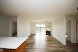 Open-concept living space featuring wood-finish flooring, a contemporary fireplace with a white mantel, and a sliding glass door to an outdoor area - 