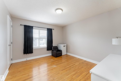 Spacious room featuring wood-finish flooring, light neutral wall paint, and a window with blinds - 10008 144 Ave, Edmonton, AB 