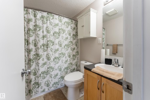 Bathroom featuring wood-finish vanity with countertop, undermount sink, and wall-mounted mirror - 10008 144 Ave, Edmonton, AB 