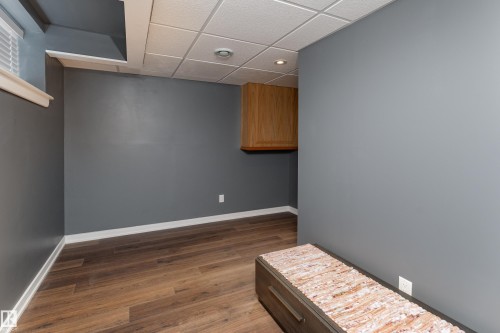 Spacious room featuring wood-finish flooring, dark gray painted walls, and white baseboards - 10008 144 Ave, Edmonton, AB 
