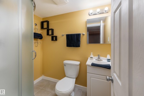 Bathroom featuring a frosted glass shower enclosure, white toilet, and a vanity with a white countertop and chrome faucet - 10008 144 Ave, Edmonton, AB 