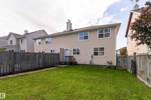 Private backyard featuring a wooden fence, manicured lawn, and a small deck with steps leading to the back entrance - 10008 144 Ave, Edmonton, AB 