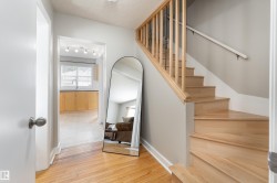 Hardwood flooring in entry with natural wood staircase featuring a banister and spindles - 