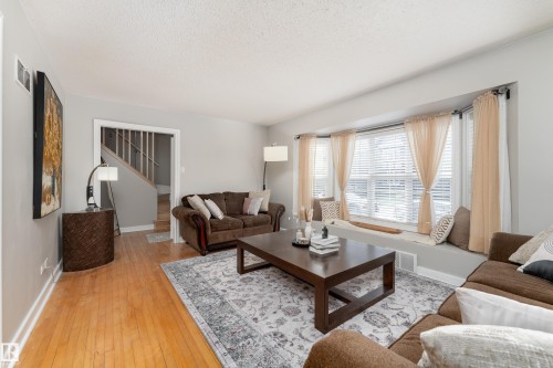 Spacious living area featuring wood-finish flooring, a broad bay window with a built-in window seat, and light gray wall paint - 10008 144 Ave, Edmonton, AB 