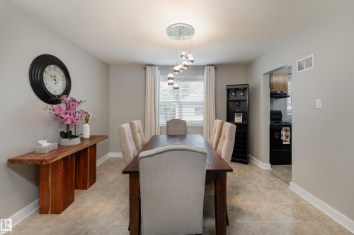 Formal dining area featuring a rectangular wood-finish table with upholstered chairs, a contemporary multi-bulb chandelier, neutral wall paint, and light-toned flooring - 10008 144 Ave, Edmonton, AB 