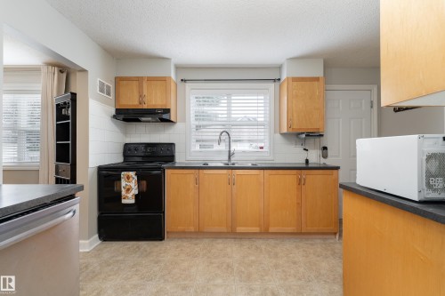 Kitchen featuring light wood cabinetry, dark countertops, white subway tile backsplash, and neutral tile flooring - 10008 144 Ave, Edmonton, AB 