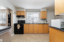 Kitchen featuring light wood cabinetry, dark countertops, white subway tile backsplash, and neutral tile flooring - 