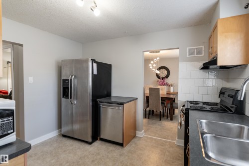 Kitchen featuring stainless steel appliances, wood-finish cabinetry, tile flooring, subway tile backsplash, and a double basin sink - 10008 144 Ave, Edmonton, AB 